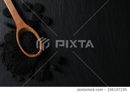 Activated charcoal powder in a wooden spoon on a dark background 106197295