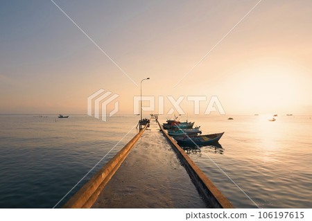 Long pier with moored boats in fishing village at sunrise. 106197615