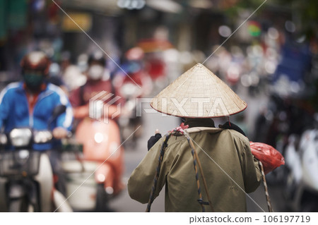 Person with traditional conical hat against traffic motorbikes on busy street. 106197719