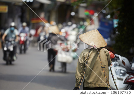 Person with traditional conical hat against traffic motorbikes on busy street. Person with traditional conical hat against traffic motorbikes on busy street. 106197720