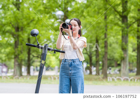 一位年輕可愛的女士在電動浮板上移動時拿著愛好相機 | 相機女孩的圖片 一位年輕可愛的女士在電動浮板上移動時拿著愛好相機 | 相機女孩的圖片 106197752