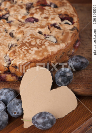 Appetizing homemade fresh plums pie on old wooden table Food concept. Empty blank in the form of a heart for writing a note, a recipe 106198095