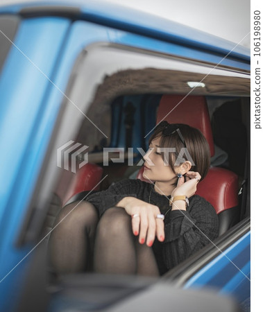 A woman kneeling in the passenger seat of a car and touching her piercing 106198980