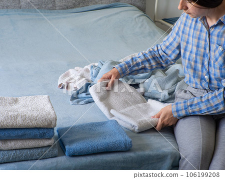 Woman folding clean terry towel in the bedroom. Organizing laundry at home. Woman folding clean terry towel in the bedroom. Organizing laundry at home. 106199208