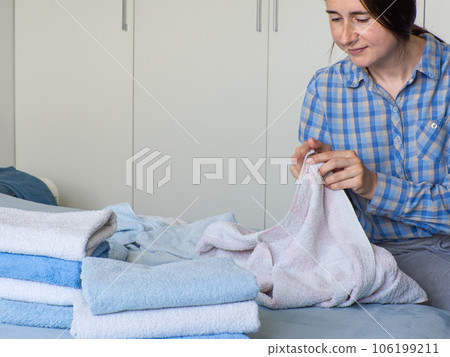 Woman folding clean terry towel in the bedroom. Organizing laundry at home. 106199211