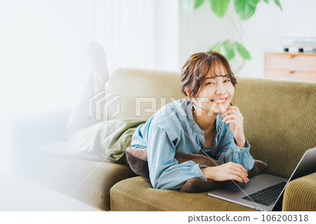 A woman using a computer while lying on the sofa A woman using a computer while lying on the sofa 106200318