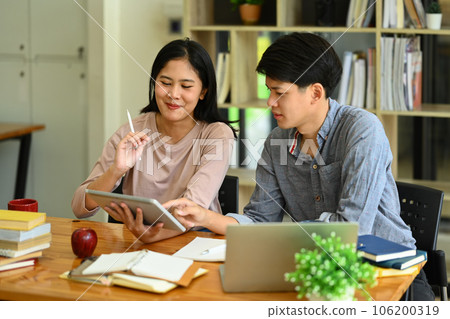Two college students using digital tablet in library, studying together for exam or research for project Two college students using digital tablet in library, studying together for exam or research for project 106200319
