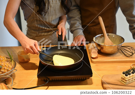 Cropped shot of young couple making pancakes on frying pan, preparing breakfast in kitchen Cropped shot of young couple making pancakes on frying pan, preparing breakfast in kitchen 106200322