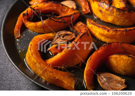 pieces of baked pumpkin with spices and garlic on a black plate 106200620