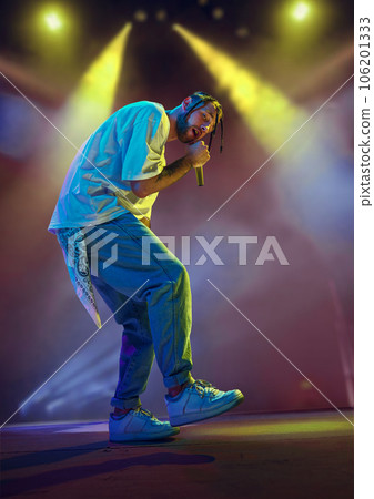 Young artistic man, musician making live concert, singing, dancing on stage over colorful neon illumination. Night club 106201333