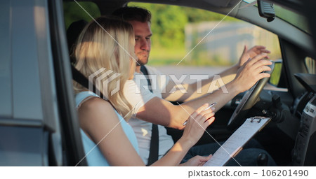 Young man and driving school instructor with clipboard talking in car. Man listening to instructor in car learning to drive. 106201490