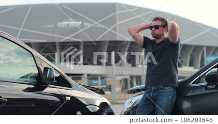 Young man in sunglasses sits stressed out after a car crash on the road. The concept of traffic accidents and insurance. 106201646