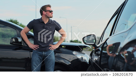 Young man in sunglasses sits stressed out after a car crash on the road. The concept of traffic accidents and insurance. Young man in sunglasses sits stressed out after a car crash on the road. The concept of traffic accidents and insurance. 106201670