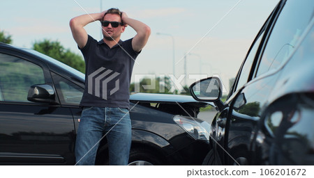 Young man in sunglasses sits stressed out after a car crash on the road. The concept of traffic accidents and insurance. Young man in sunglasses sits stressed out after a car crash on the road. The concept of traffic accidents and insurance. 106201672