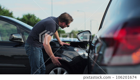 Young man in sunglasses sits stressed out after a car crash on the road. The concept of traffic accidents and insurance. 106201674