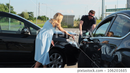 Young caucasian man and woman talking and gesturing looking at broken cars on roadside. Stressed male and female drivers arguing on road accident. 106201685