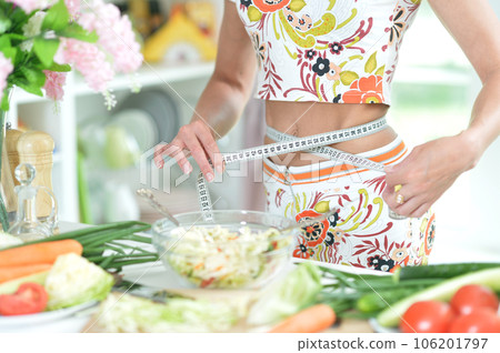 A girl measures her waist with a centimeter in the kitchen. A girl measures her waist with a centimeter in the kitchen. 106201797