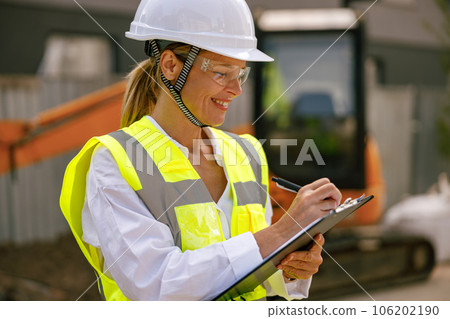 Professional female engineer in protective helmet making notes on construction site Professional female engineer in protective helmet making notes on construction site 106202190