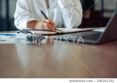 Close up of business woman working on laptop, making notes in modern office interior Close up of business woman working on laptop, making notes in modern office interior 106202192
