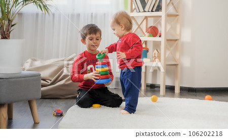 Little baby boy playing in toys with his older brother on carpet in living room. Concept of child education, baby development, family playing games. Little baby boy playing in toys with his older brother on carpet in living room. Concept of child education, baby development, family playing games. 106202218