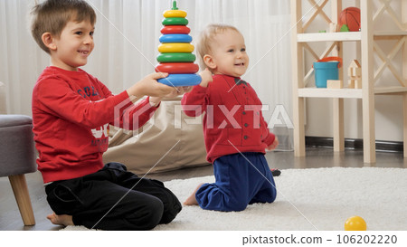 Two happy little boys smiling and cheering after assembling toy tower on carpet in living room. Concept of child education, baby development, family playing games. Two happy little boys smiling and cheering after assembling toy tower on carpet in living room. Concept of child education, baby development, family playing games. 106202220
