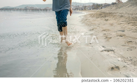 A joyful little boy running along the sandy beach and splashing water. Happiness and excitement of traveling with kids on a summer holiday. 106202381