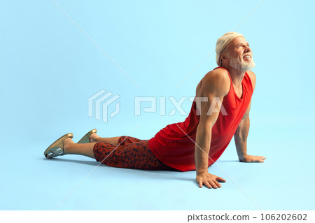 Horizontal image of middle-aged grey-head man with beard doing exercises on floor. Yoga cat pose. Recreation, relaxation, body rest. 106202602