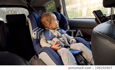 Little baby by sitting in the safety child car seat and looking out of the open window. Concept of kids traveling, baby safety, children going by car. Little baby by sitting in the safety child car seat and looking out of the open window. Concept of kids traveling, baby safety, children going by car. 106202607