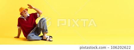 Banner. Flyer. Stylish attractive mature grey-hair man with beard sitting on floor against yellow studio background. Copy space for ad. Banner. Flyer. Stylish attractive mature grey-hair man with beard sitting on floor against yellow studio background. Copy space for ad. 106202622