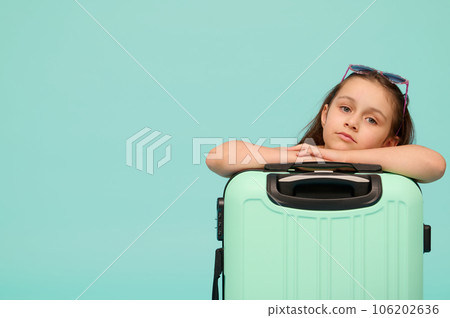 Beautiful little child girl looking at camera, posing with blue suitcase, isolated over studio background. Copy ad space 106202636