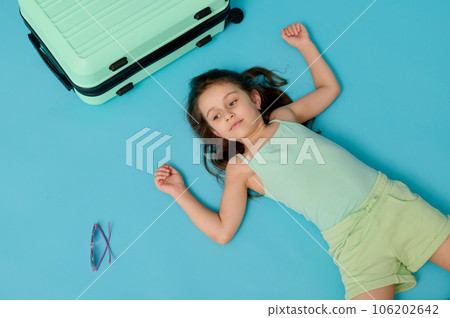 Little traveler girl going for weekend getaway, lying with her suitcase, meditating in lotus pose, isolated background 106202642