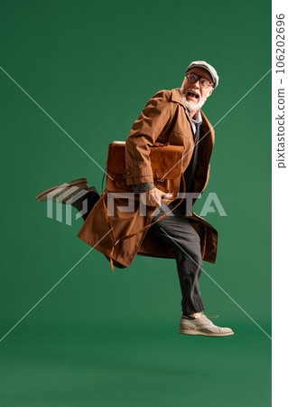 Full length portrait of running senior man with beard, detective wearing vintage hat and suit with big business bag looks scared on green background. Full length portrait of running senior man with beard, detective wearing vintage hat and suit with big business bag looks scared on green background. 106202696
