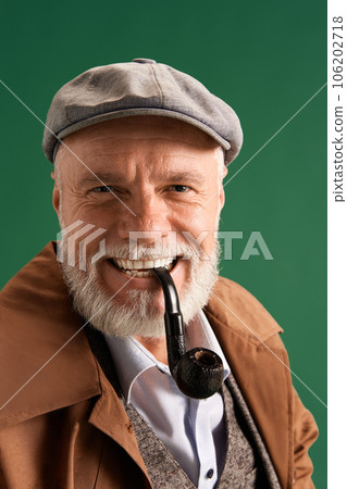 Portrait of confident, positive detective wearing vintage hat, elegance suit with pipe in mouth on green color background. Portrait of confident, positive detective wearing vintage hat, elegance suit with pipe in mouth on green color background. 106202718