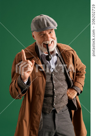 Photo of confident detective with hands on hips wearing vintage hat, elegance suit with pipe in mouth on green color background Photo of confident detective with hands on hips wearing vintage hat, elegance suit with pipe in mouth on green color background 106202719