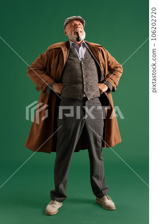 Photo of confident detective with hands on hips wearing vintage hat, elegance suit with pipe in mouth on green color background Photo of confident detective with hands on hips wearing vintage hat, elegance suit with pipe in mouth on green color background 106202720
