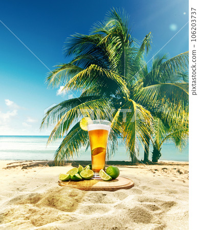Glass with delicious lager beer with lime appetizers on sand near palm with blue sky and ocean background 106203737