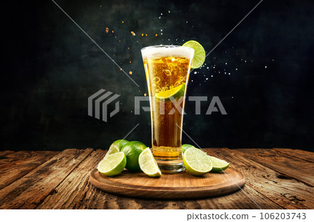 Glass with lager, chill, delicious beer with lime appetizers on wooden table against black background 106203743