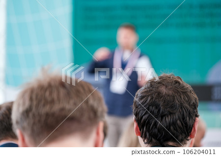 Back view of male attendee taking part in conference listening to presentation of speaker on stage 106204011