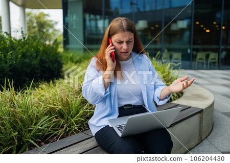 Sad Caucasian student freelancer 30s woman rest use laptop pc computer talk by mobile cell phone look, outdoors sits at city cafe against blurred city building. She is keyboarding on laptop. Freelance Sad Caucasian student freelancer 30s woman rest use laptop pc computer talk by mobile cell phone look, outdoors sits at city cafe against blurred city building. She is keyboarding on laptop. Freelance 106204480