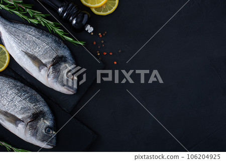 Fresh raw dorado fish on black stone background with spices, rosemary and lemon. Culinary seafood background with copy space. Two Dorada fishes on shale boards. Fresh raw dorado fish on black stone background with spices, rosemary and lemon. Culinary seafood background with copy space. Two Dorada fishes on shale boards. 106204925
