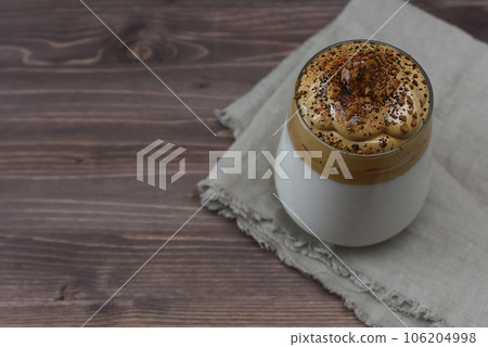 Dalgona coffee on a wooden background with copy space. Homemade dalgona coffee in glass with milk. Trendy fluffy creamy whipped coffee on wooden stand. 106204998