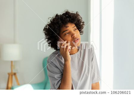 African american girl talking on smartphone at home indoor. Young woman with cell phone chatting with friends. Smiling teen girl making answering call by cellphone. Lady having conversation by mobile African american girl talking on smartphone at home indoor. Young woman with cell phone chatting with friends. Smiling teen girl making answering call by cellphone. Lady having conversation by mobile 106206021