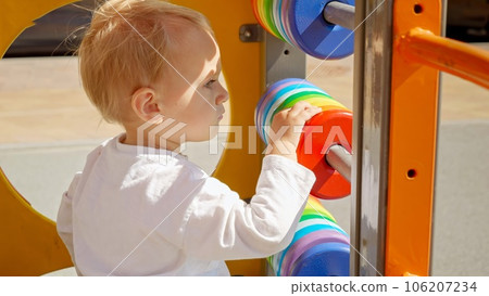 Portrait of blonde baby boy playing on colorful wooden playground outdoors. Children developments, kids education, baby learning. 106207234