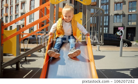Cute baby boy sitting on the top of slide and riding down. Happy parenting, family having time together, kids and parents outdoors. 106207282