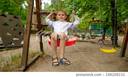 Little boy smiling as swinging on swing at adventure park. Kids playing outdoors, children having fun, summer vacation and holiday. Little boy smiling as swinging on swing at adventure park. Kids playing outdoors, children having fun, summer vacation and holiday. 106208132