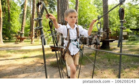 Little boy walking over rope bridge at outdoor amusement park. Active childhood, healthy lifestyle, kids playing outdoors, children in nature. 106208143