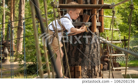Little boy climbing over ropes and bridges in summer scout camp. Active childhood, healthy lifestyle, kids playing outdoors, children in nature. Little boy climbing over ropes and bridges in summer scout camp. Active childhood, healthy lifestyle, kids playing outdoors, children in nature. 106208156