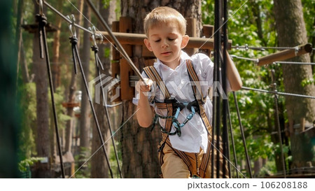 Portrait of cute boy holding safety rope at outdoor extreme adventure park. Active childhood, healthy lifestyle, kids playing outdoors, children in nature. 106208188