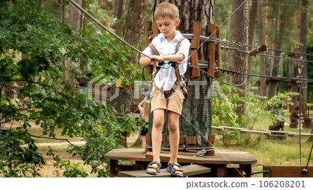 Little concentrated boy lookin down his feet while crossing wobbly rope bridge in extreme park 106208201