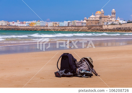 Two backpacks, a hat and sandals lie on the sand on the coastline against the backdrop of the sea. Two backpacks, a hat and sandals lie on the sand on the coastline against the backdrop of the sea. 106208726